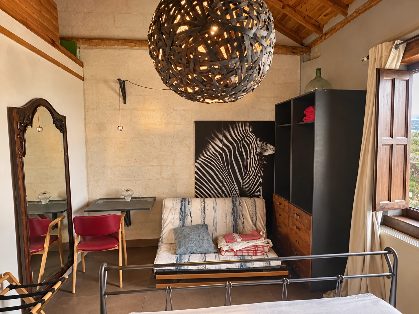 Dormitorio con lámpara artesanal esférica, espejo antiguo y cama de forja
