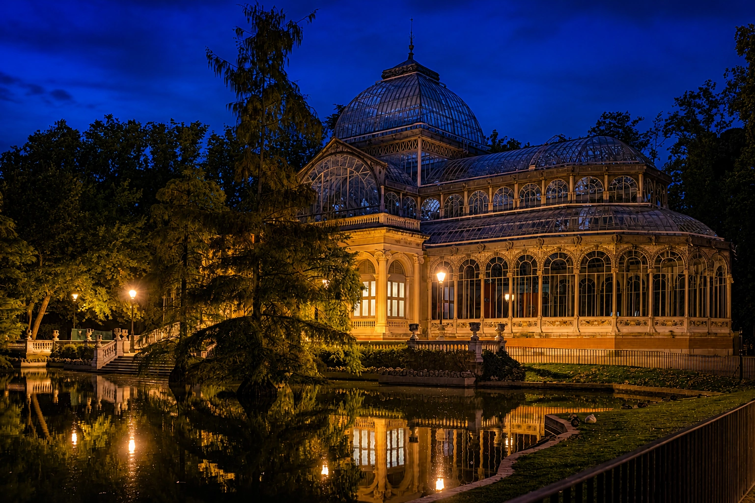Palacio de Cristal del Retiro de Madrid iluminado de noche junto al estanque