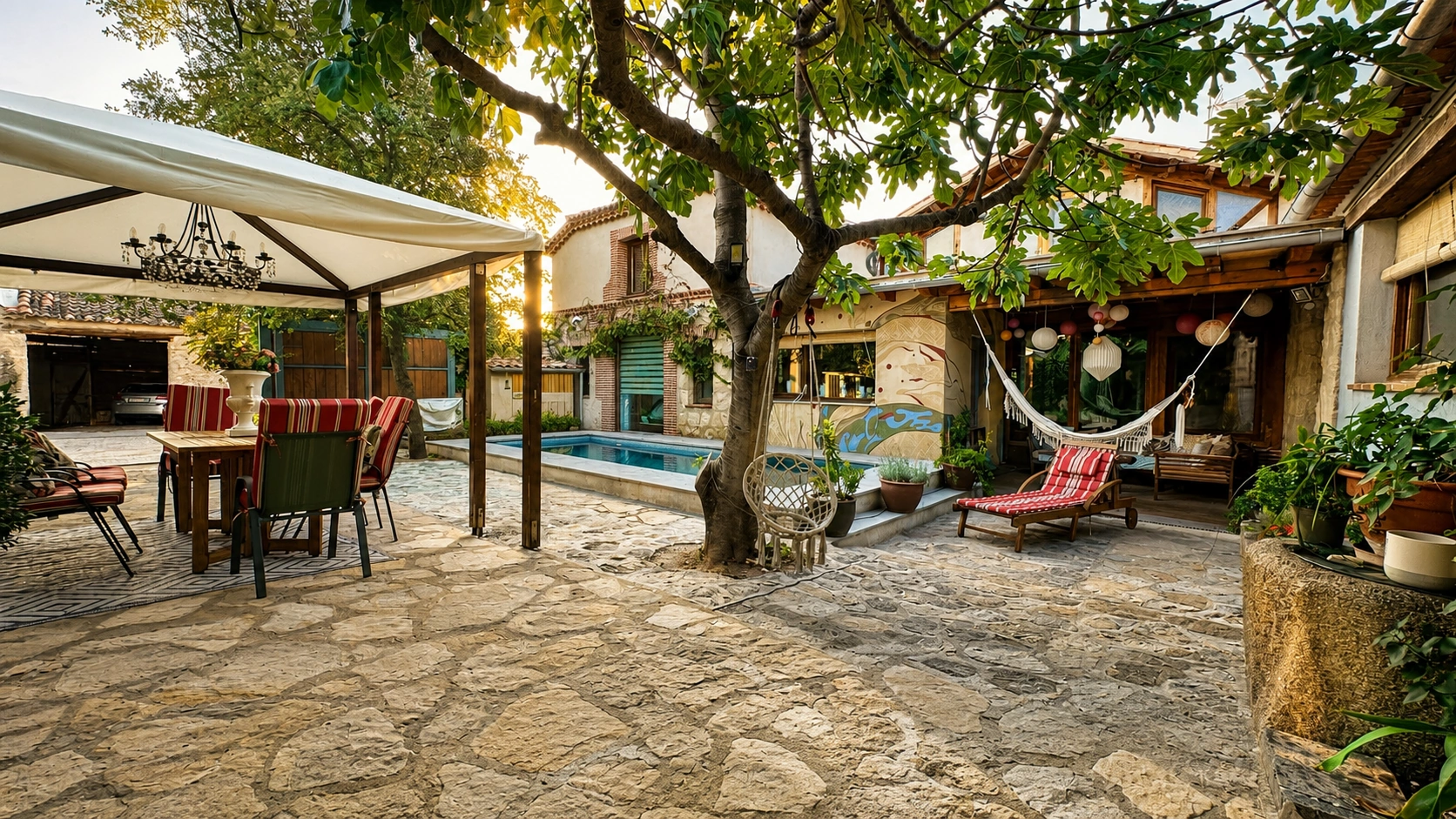 Patio empedrado con pérgola, hamacas y piscina de la casa rural Viento de Ladera en Segovia